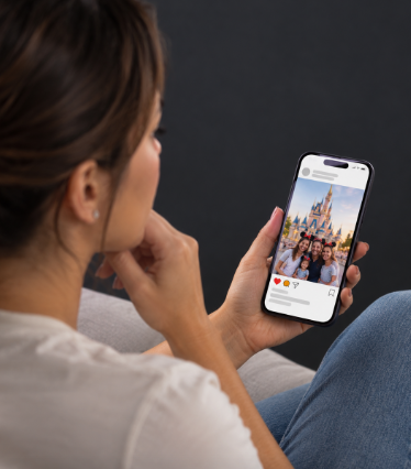 Mãe sentada no sofá, pensativa, com a mão no queixo e o celular na outra mão